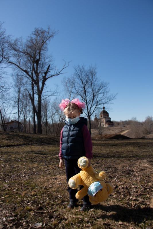 A little girl in a medical mask stands on the street during the COVID 19 Coronavirus pandemic. She is holding a toy teddy bear, who is also wearing a medical mask.  CREDIT Nik Anderson, www.vperemen.com