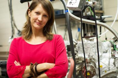 Physics graduate student Charlotte Sanders' research with professor Ken Shih helped develop the world's smallest nanolaser. She stands here with a molecular beam epitaxy machine that she designed and built in collaboration with the Department of Physics Machine Shop and with assistance from co-author Dr. Jisun Kim. The machine is used to create a smooth silver thin film critical to the function of the laser.  Credit: Alex Wang