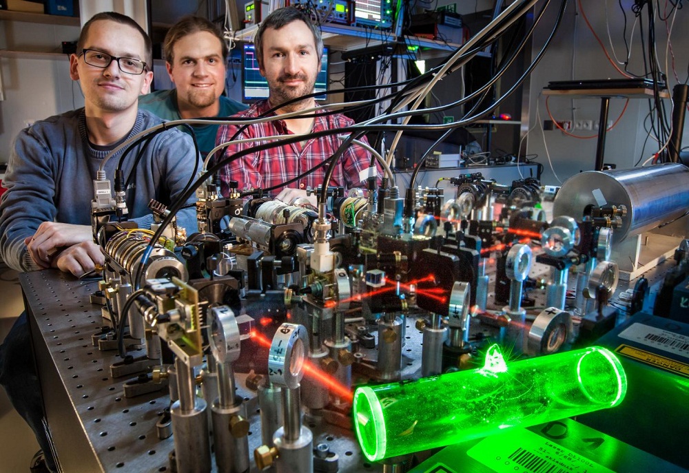 An atomic memory (glowing green), made at the Faculty of Physics at the University of Warsaw, can be used to store quantum information in telecomunication purposes. From left to right: Michał Dąbrowski, Radek Chrapkiewicz and Wojciech Wasilewski.  Credit: ©FUW, R. Chrapkiewicz