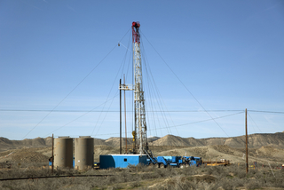 A tall drill rig and drill bits with liquid storage tanks at the Rangely Oil Field in 2014. | milehightraveler/ iStock